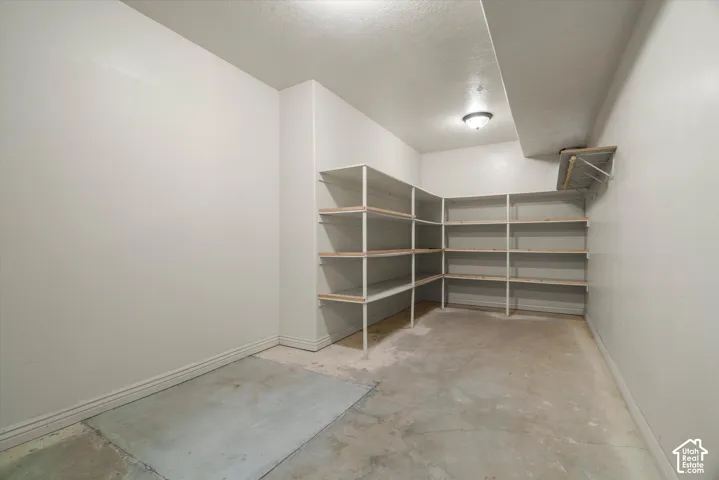 Spacious storage room featuring extensive built-in shelving, concrete flooring, and a ceiling-mounted light fixture