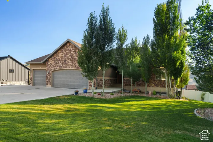 Stone facade residence featuring an attached three-car garage with arched entry, a concrete driveway, and mature landscaping