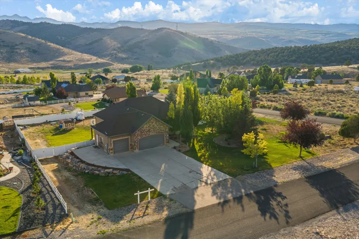 Stone and stucco exterior residence featuring a multi-car garage, concrete driveway, and landscaped front yard with mature trees