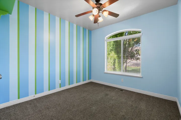 Carpeted room featuring a large arched window with horizontal blinds, a ceiling fan with integrated lighting, and a wall with blue and green vertical stripes