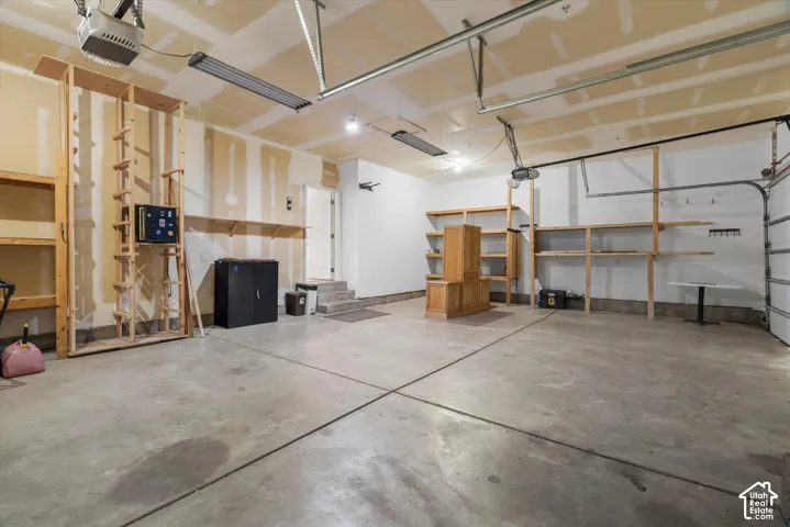 Spacious garage featuring a concrete floor, overhead lighting, garage door opener mechanisms, and extensive built-in wooden shelving units for organization