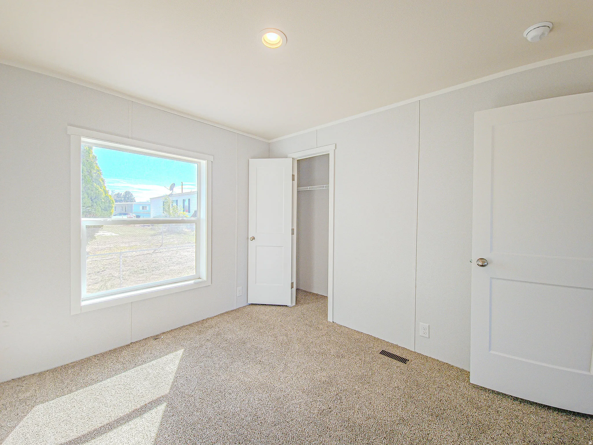 Recessed ceiling lighting, white panel doors, neutral carpeting, and a window with white trim