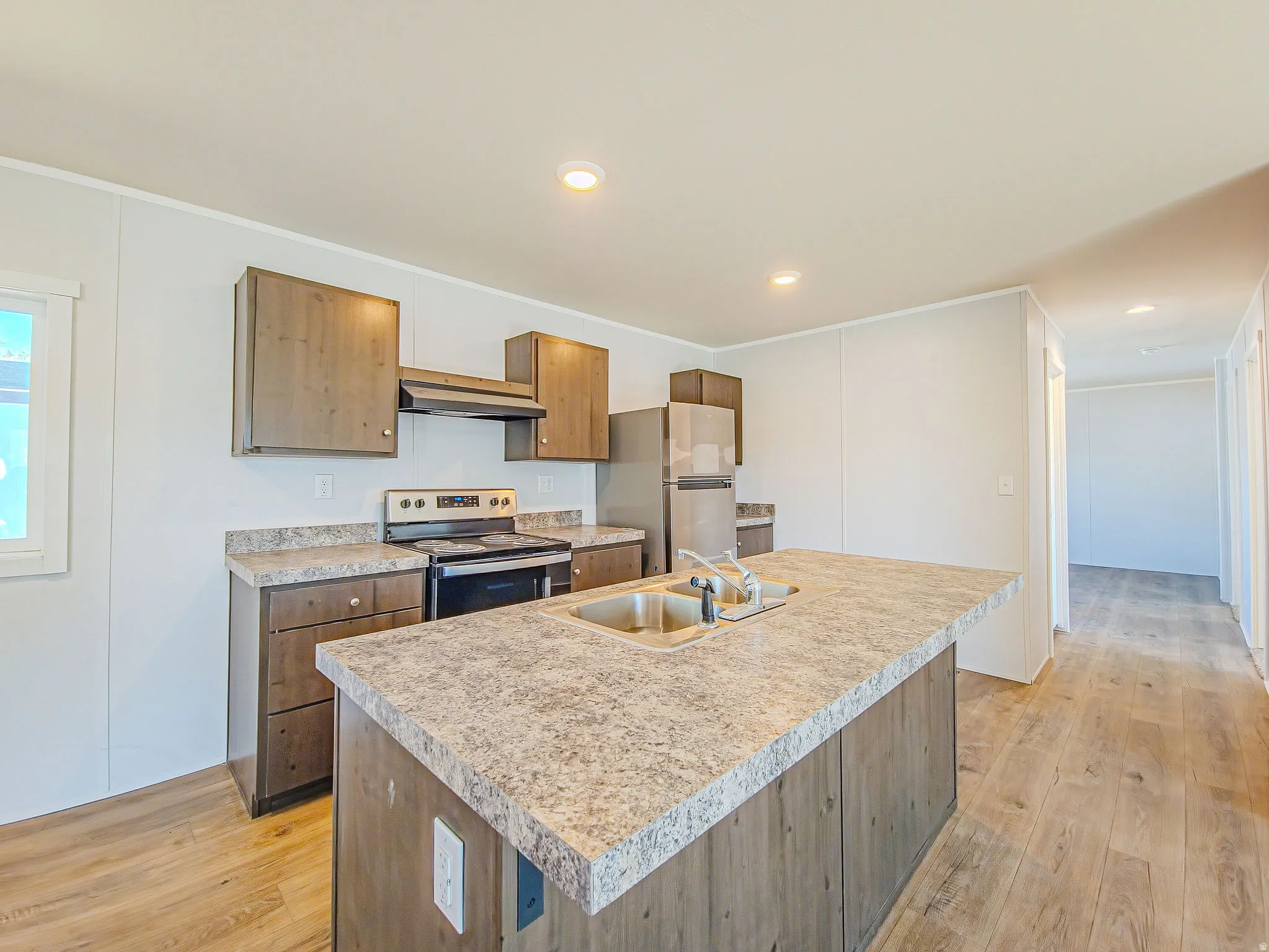 Kitchen featuring wood-finish cabinetry, stainless steel appliances, a center island with an integrated sink, and wood-finish flooring