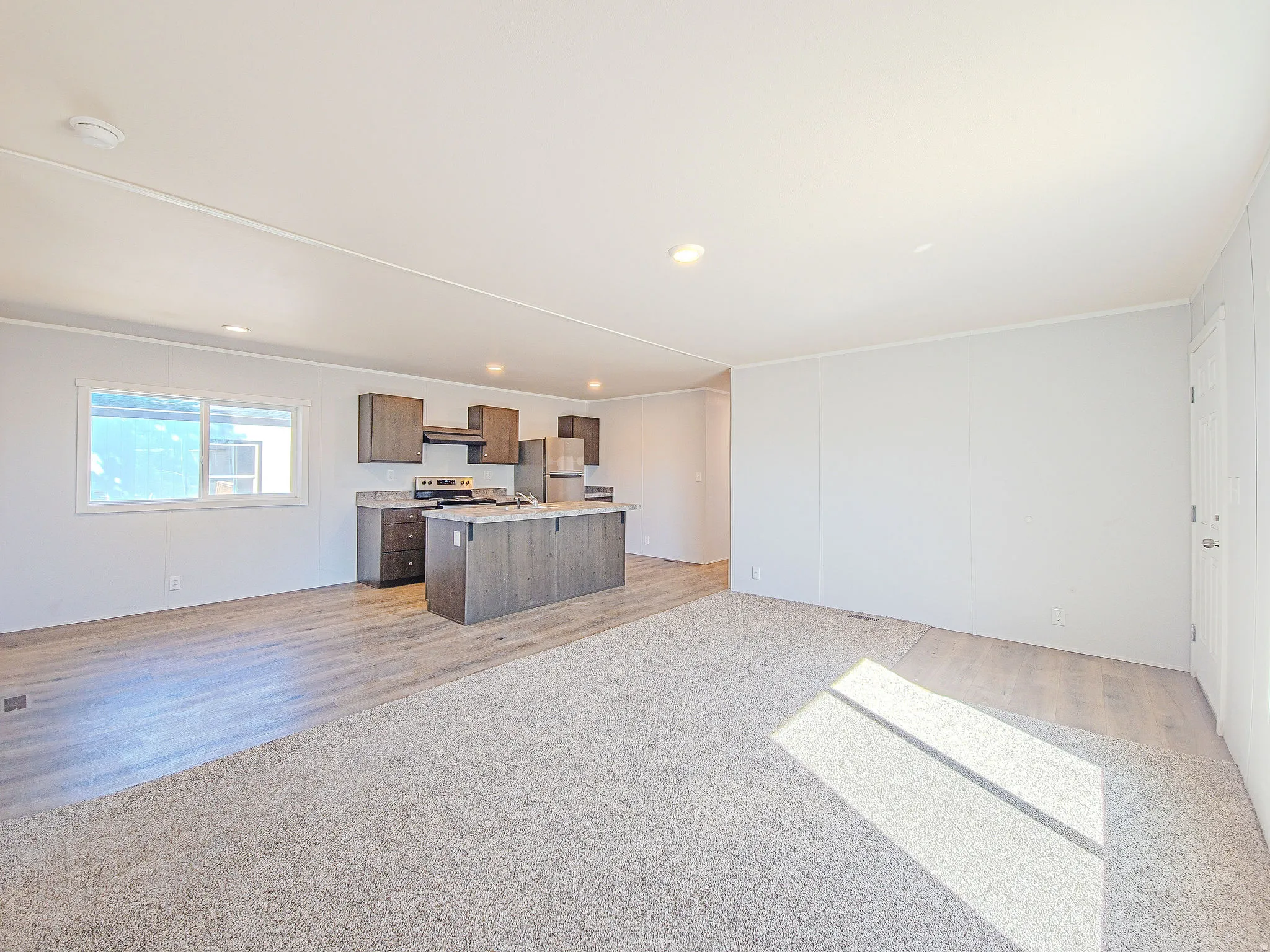 Open-concept living space featuring wood-finish flooring, recessed lighting, and a modern kitchen with an island and stainless steel appliances