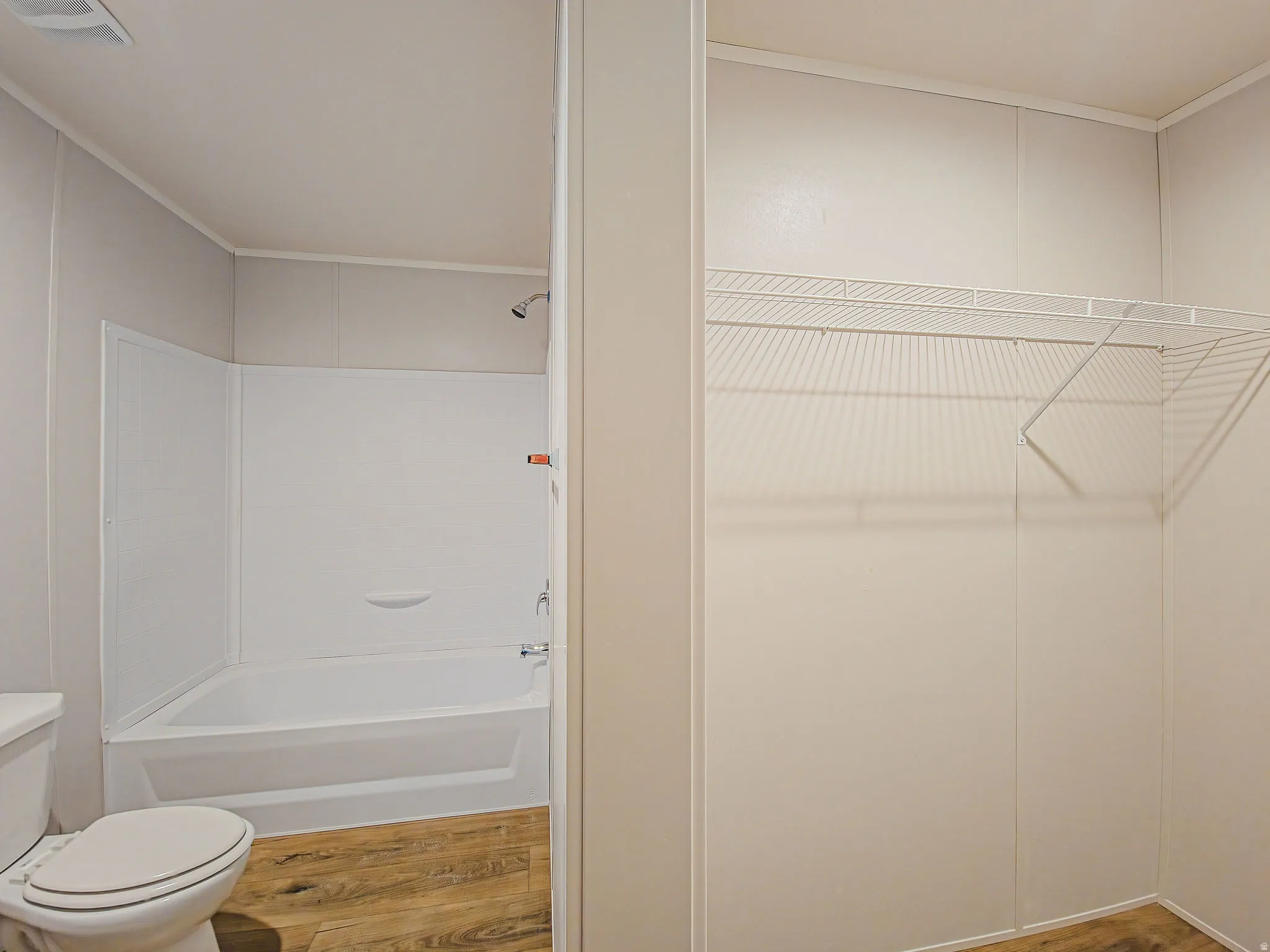 Full bathtub with shower fixture, wood-finish flooring, and wire shelving system