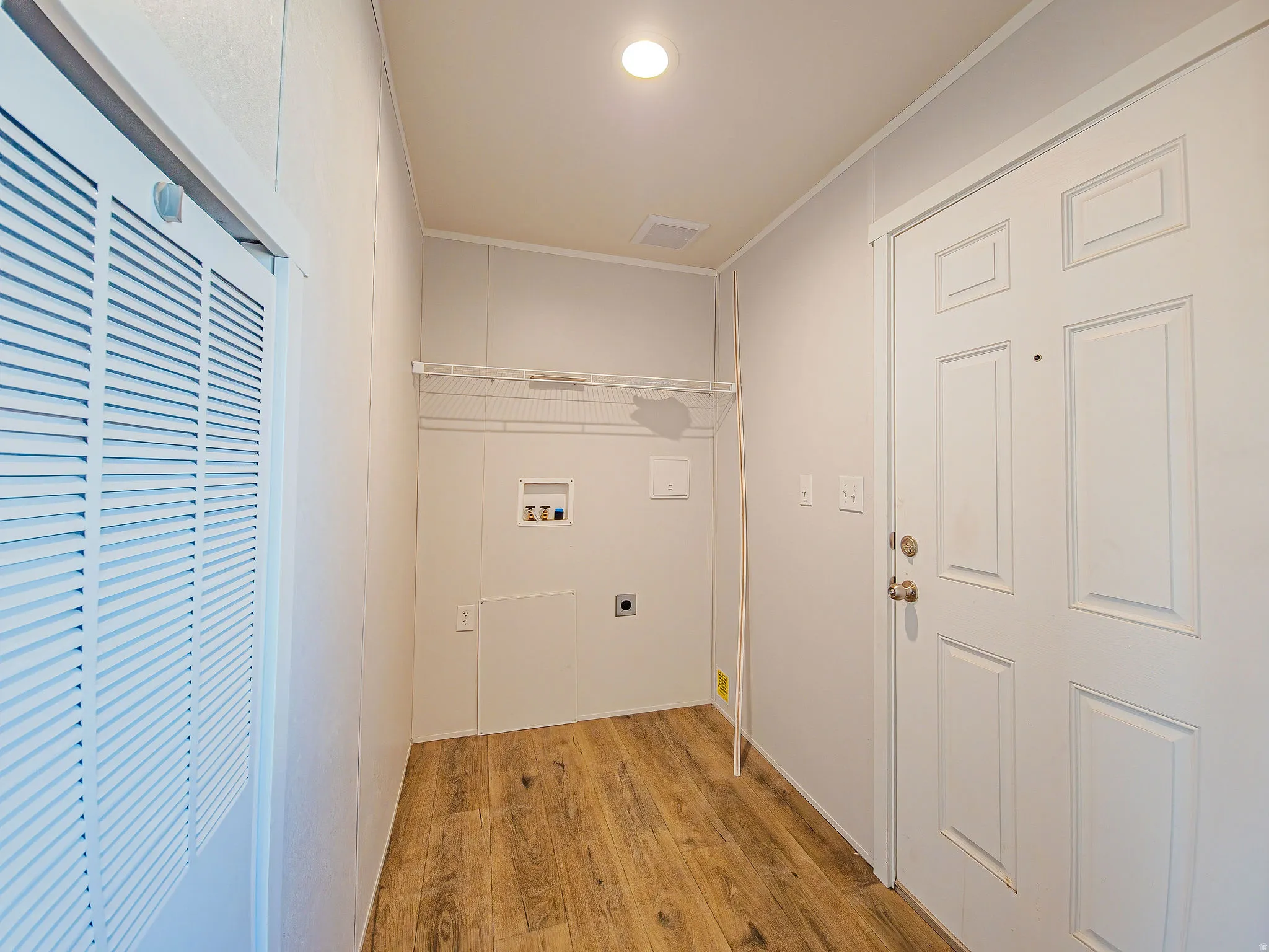 Dedicated laundry area with hookups, wood-finish flooring, and a wire shelving unit
