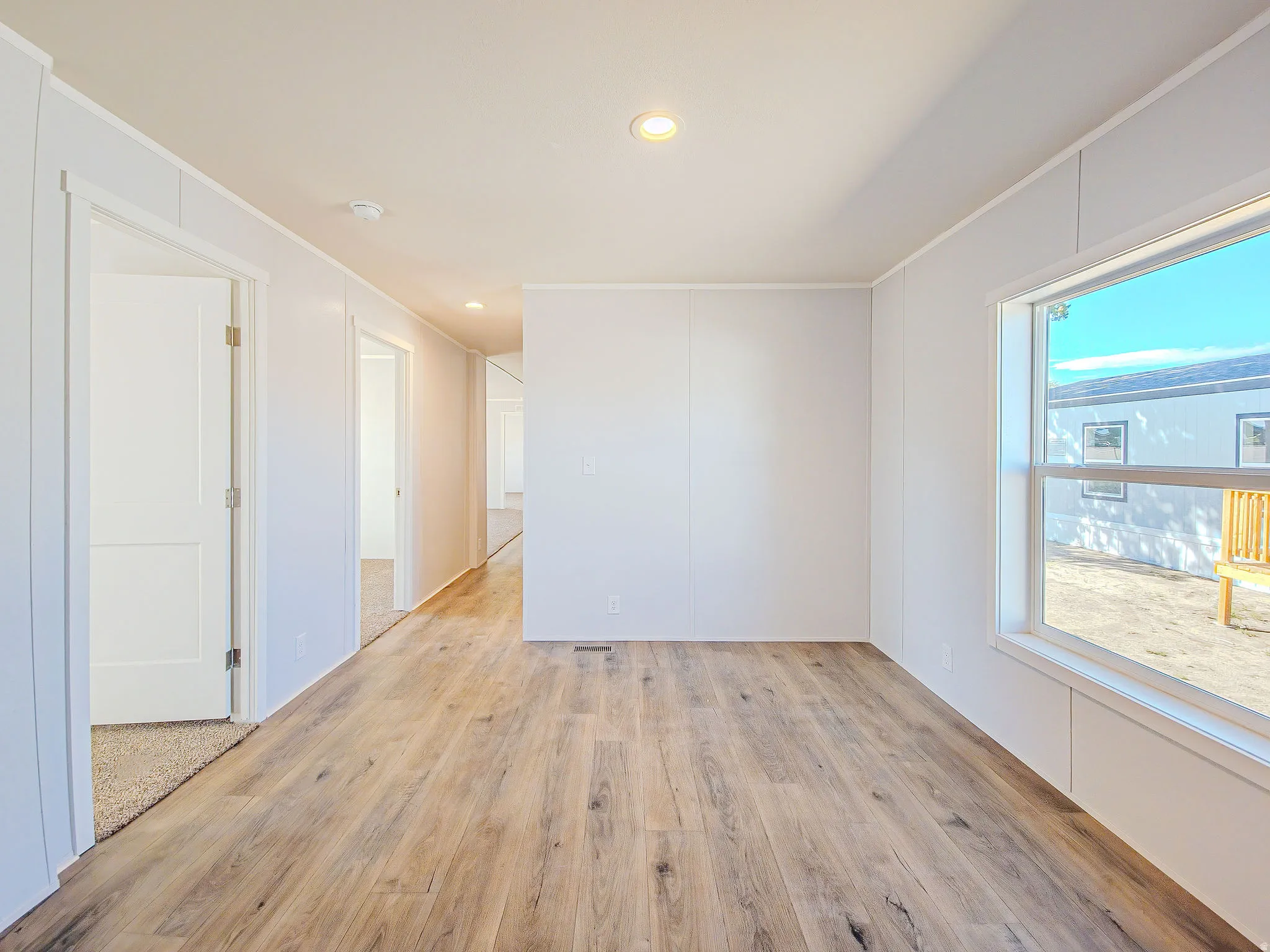 Recessed lighting illuminating wood-finish flooring, white paneled walls, and a large window