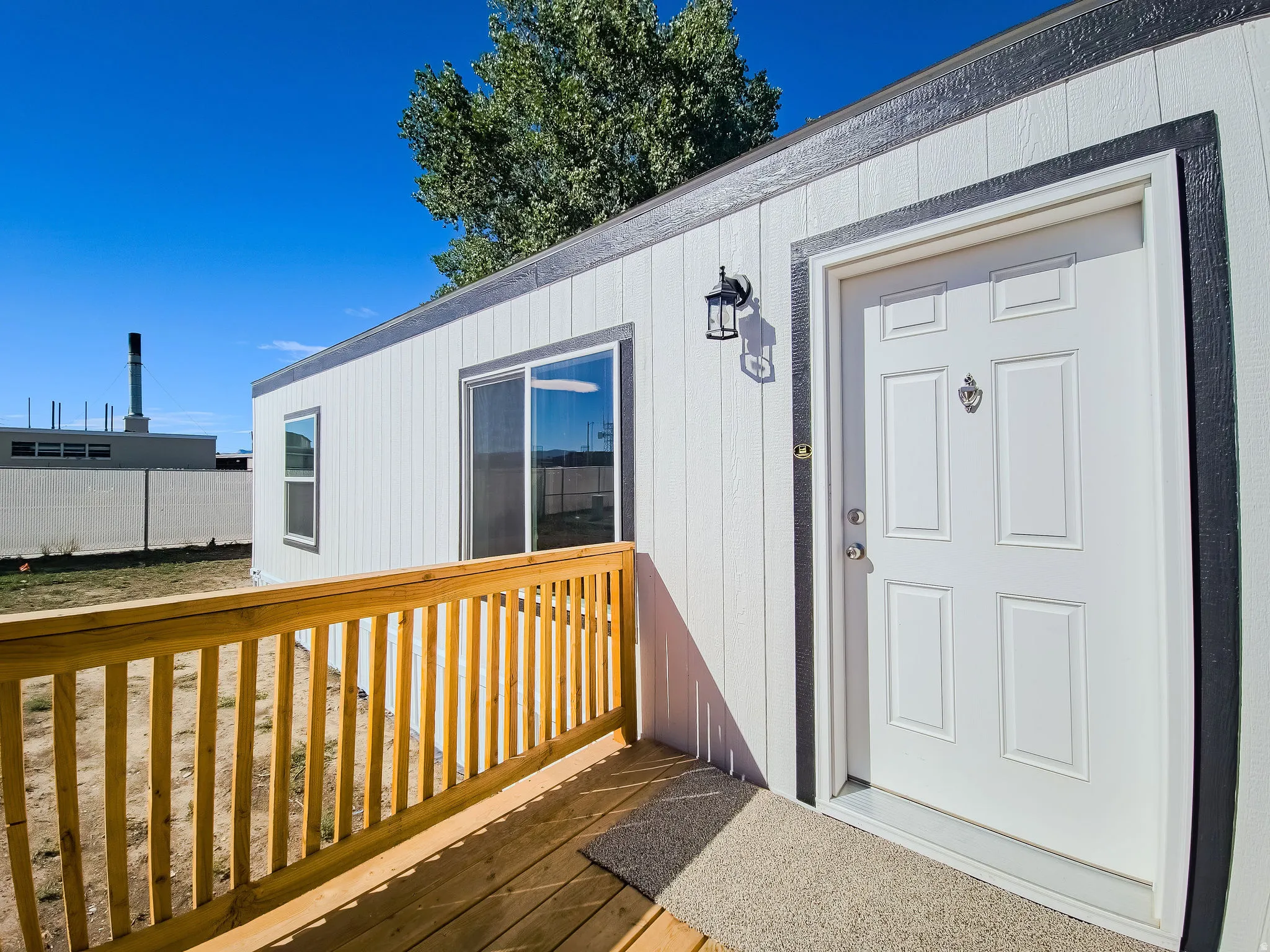 White exterior siding with dark trim accents, wooden deck with railing, sliding glass door, and a paneled entry door with an exterior light fixture