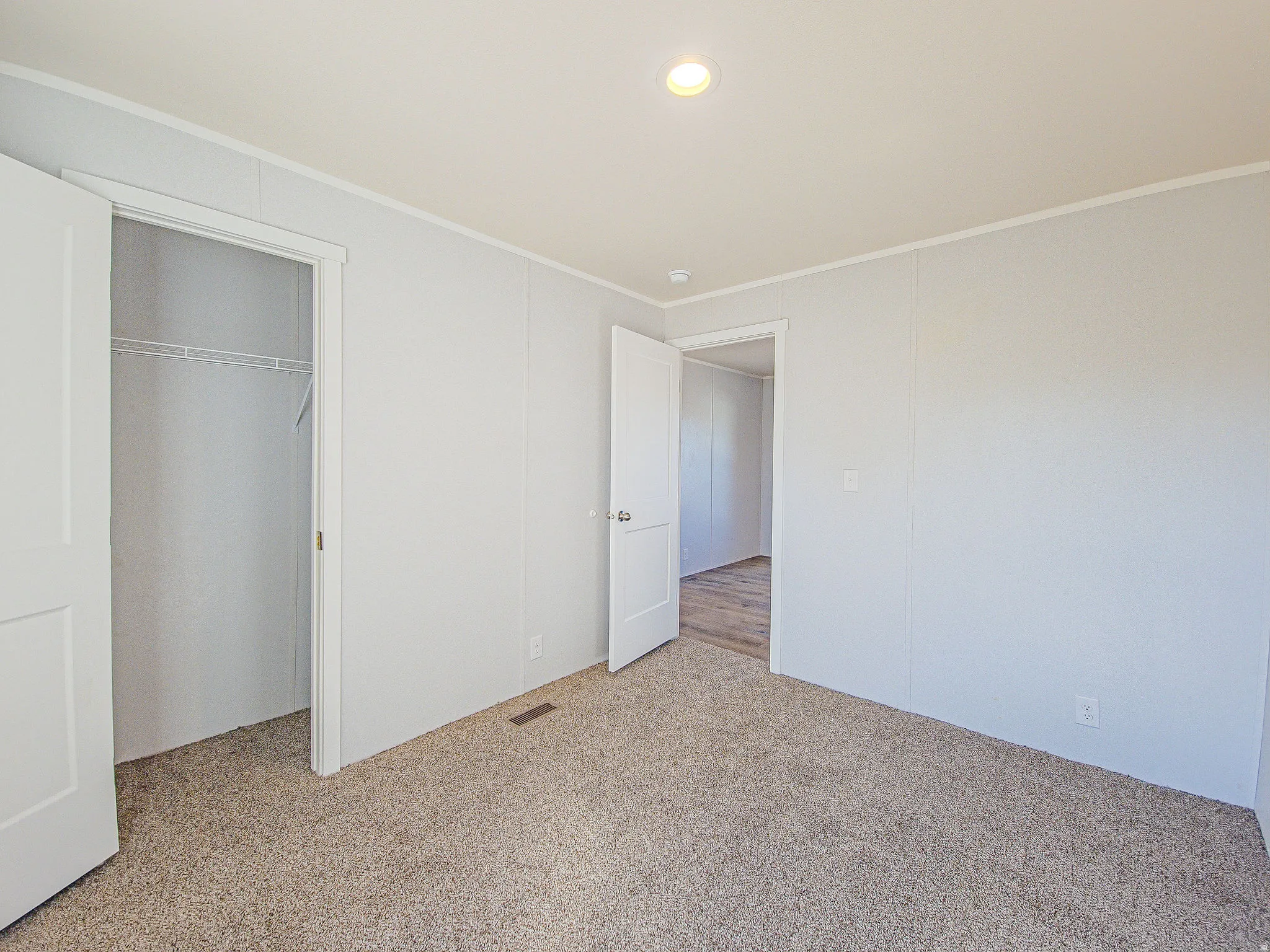 Neutral-toned carpet flooring, recessed ceiling light fixture, white panel walls, and an open doorway