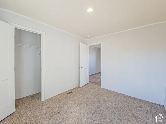 Neutral-toned carpet flooring, recessed ceiling light fixture, white panel walls, and an open doorway