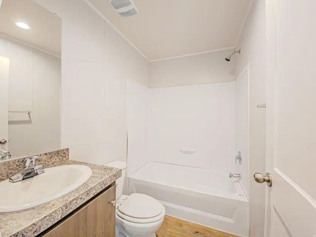 Bathroom featuring a shower-tub combination with white surround, a toilet, a vanity with a counter, and a sink with a chrome faucet
