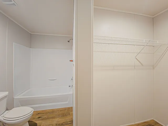 Full bathtub with shower fixture, wood-finish flooring, and wire shelving system