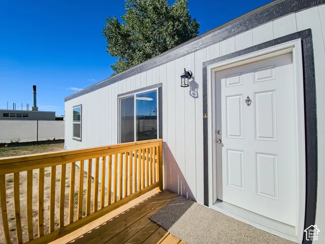 White exterior siding with dark trim accents, wooden deck with railing, sliding glass door, and a paneled entry door with an exterior light fixture