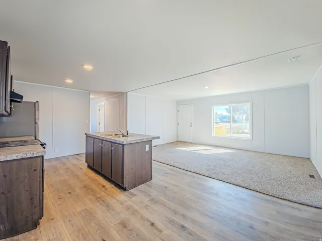 Wood-finish flooring, central kitchen island with integrated sink, recessed lighting, and a large window
