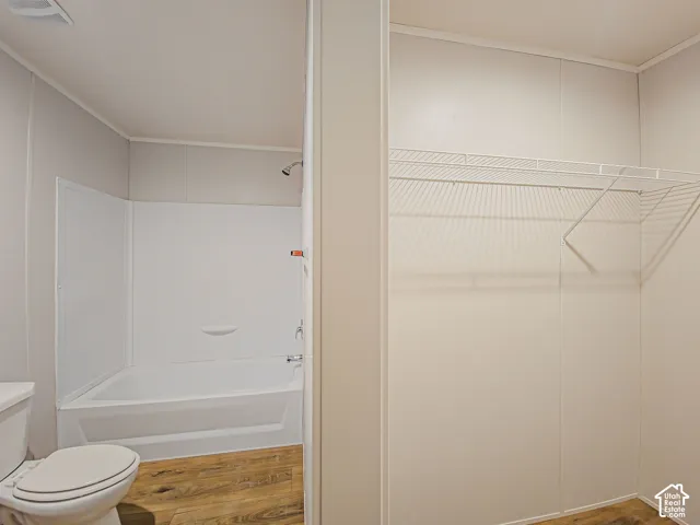 Full bathtub with shower fixture, wood-finish flooring, and wire shelving system