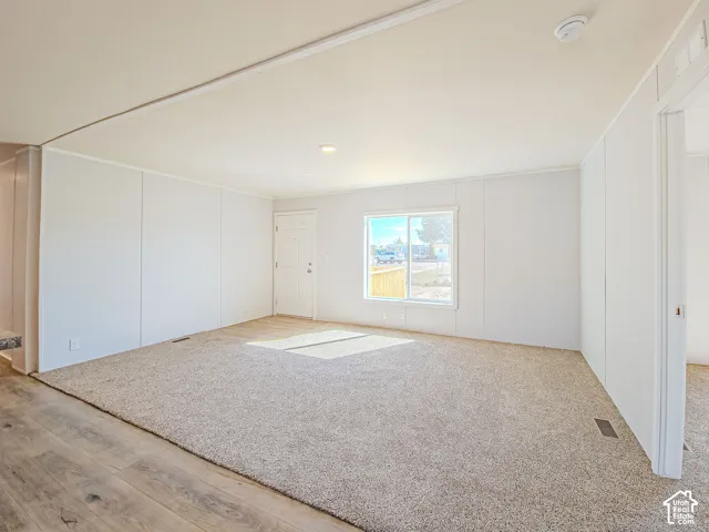 Expansive living area featuring carpet flooring, wood-finish flooring, a white paneled entrance door, a double-pane window, and recessed ceiling lighting