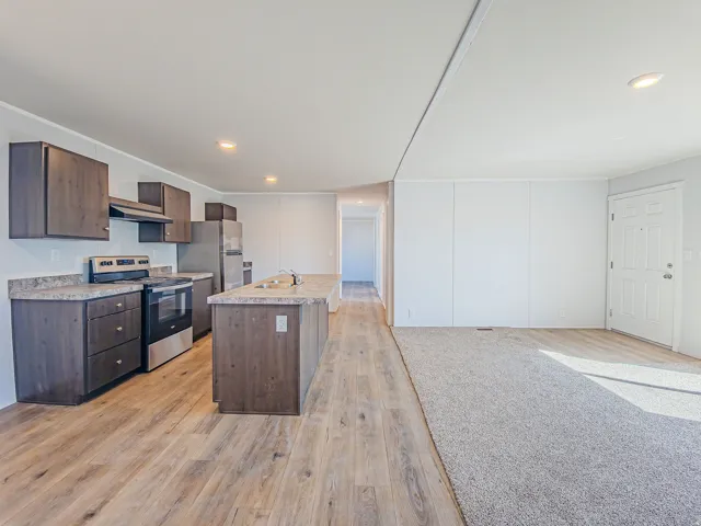 Kitchen featuring wood-finish flooring, dark wood-finish cabinetry, stainless steel appliances, and a central island with a sink