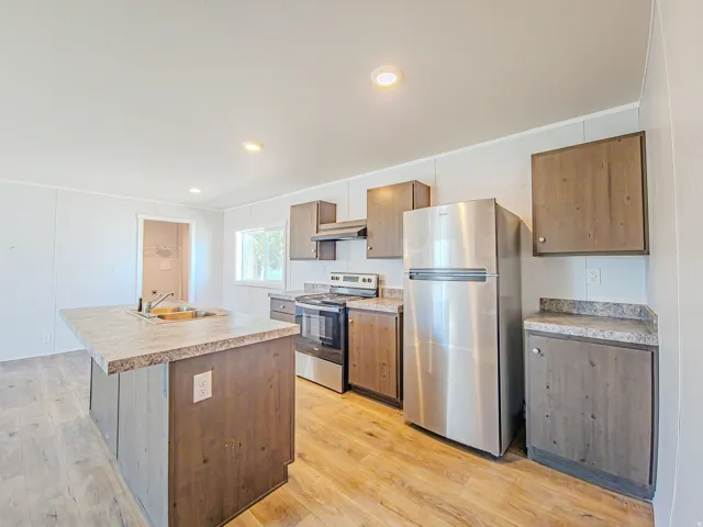 Kitchen featuring wood-finish flooring, recessed lighting, a kitchen island with a sink, stainless steel appliances, and wood-finish cabinetry