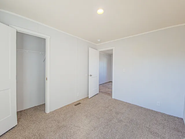 Neutral-toned carpet flooring, recessed ceiling light fixture, white panel walls, and an open doorway