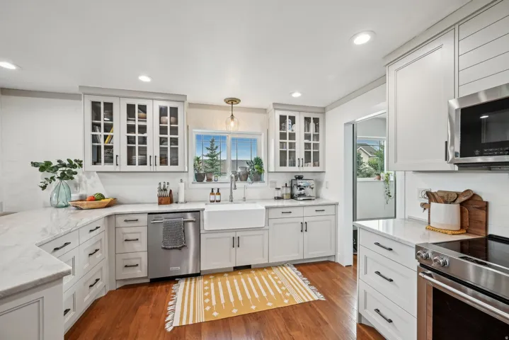 Contemporary kitchen featuring white cabinetry, light countertops, wood-finish flooring, a farmhouse sink, and stainless steel appliances