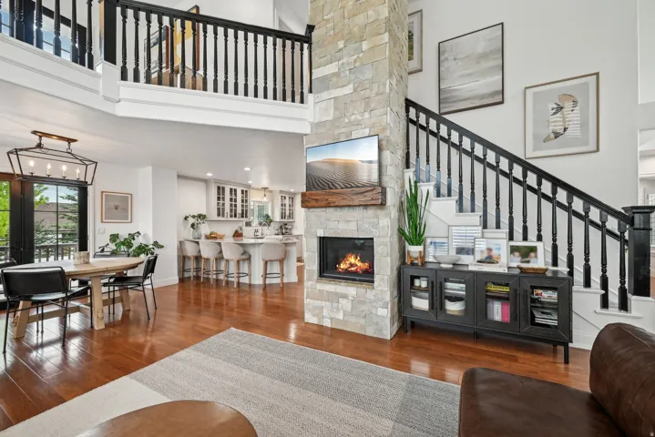 Two-story living area featuring a stone-clad fireplace with a wood mantel, wood-finish flooring, and a second-story interior balcony