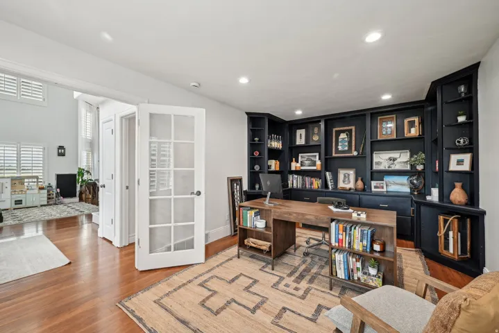Dedicated office space featuring extensive built-in shelving, wood-finish flooring, recessed lighting, and French doors