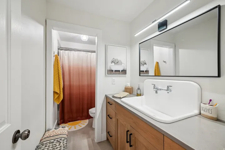 Bathroom featuring a large wall-mounted mirror, linear vanity light fixture, and a spacious trough sink