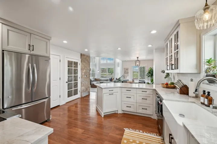 Gourmet kitchen featuring a farmhouse sink, stainless steel refrigerator, white shaker cabinetry, stone countertops, and wood-finish flooring
