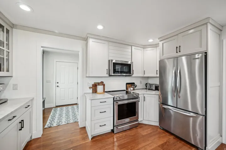 Kitchen featuring white shaker cabinetry, stainless steel appliances, marble-finish countertops, warm wood flooring, and recessed lighting