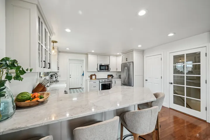 Spacious kitchen featuring an extended peninsula with a light-toned countertop, white cabinetry with glass-front accents, recessed lighting, stainless steel appliances, and wood-finish flooring