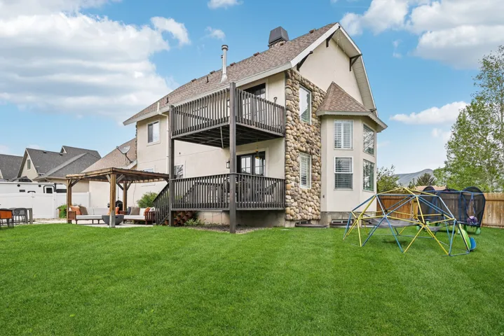 Expansive backyard featuring a manicured lawn, a two-story deck with dark wood railings, and a lower-level patio area with a pergola