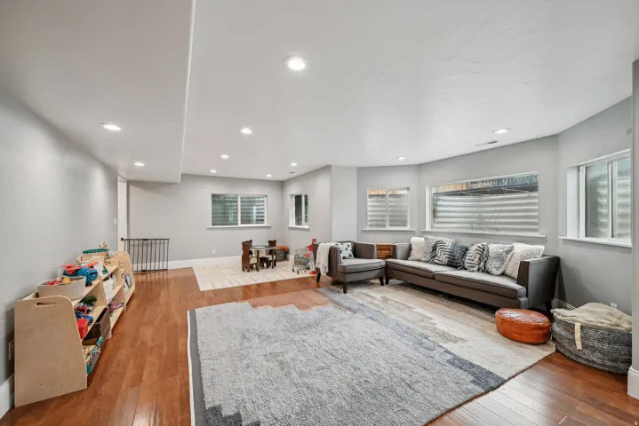 Spacious lower-level area featuring recessed lighting, light gray walls, wood-finish flooring, and multiple window wells providing natural light