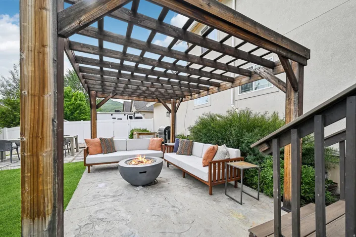 Expansive stamped concrete patio featuring a wood pergola, built-in fire pit, and direct access to a manicured lawn