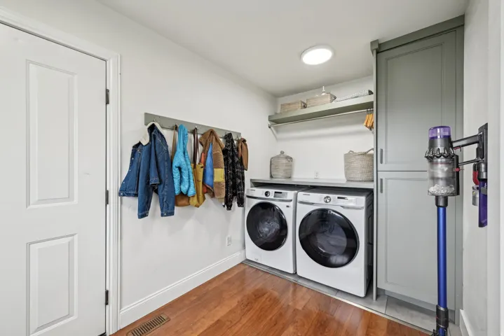 Dedicated laundry area featuring wood-finish flooring, a full-size washer and dryer, an integrated countertop, open shelving, and built-in cabinetry with a storage rack