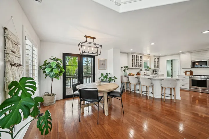 Open-concept living space with hardwood flooring, a modern kitchen island with seating, stainless steel appliances, a geometric light fixture, and black-framed French doors leading to an outdoor area