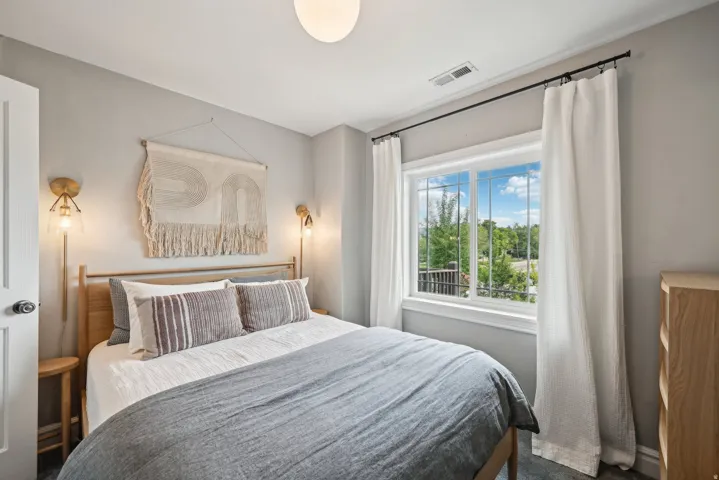 Bright bedroom featuring a large window with white trim, recessed lighting, and light gray walls