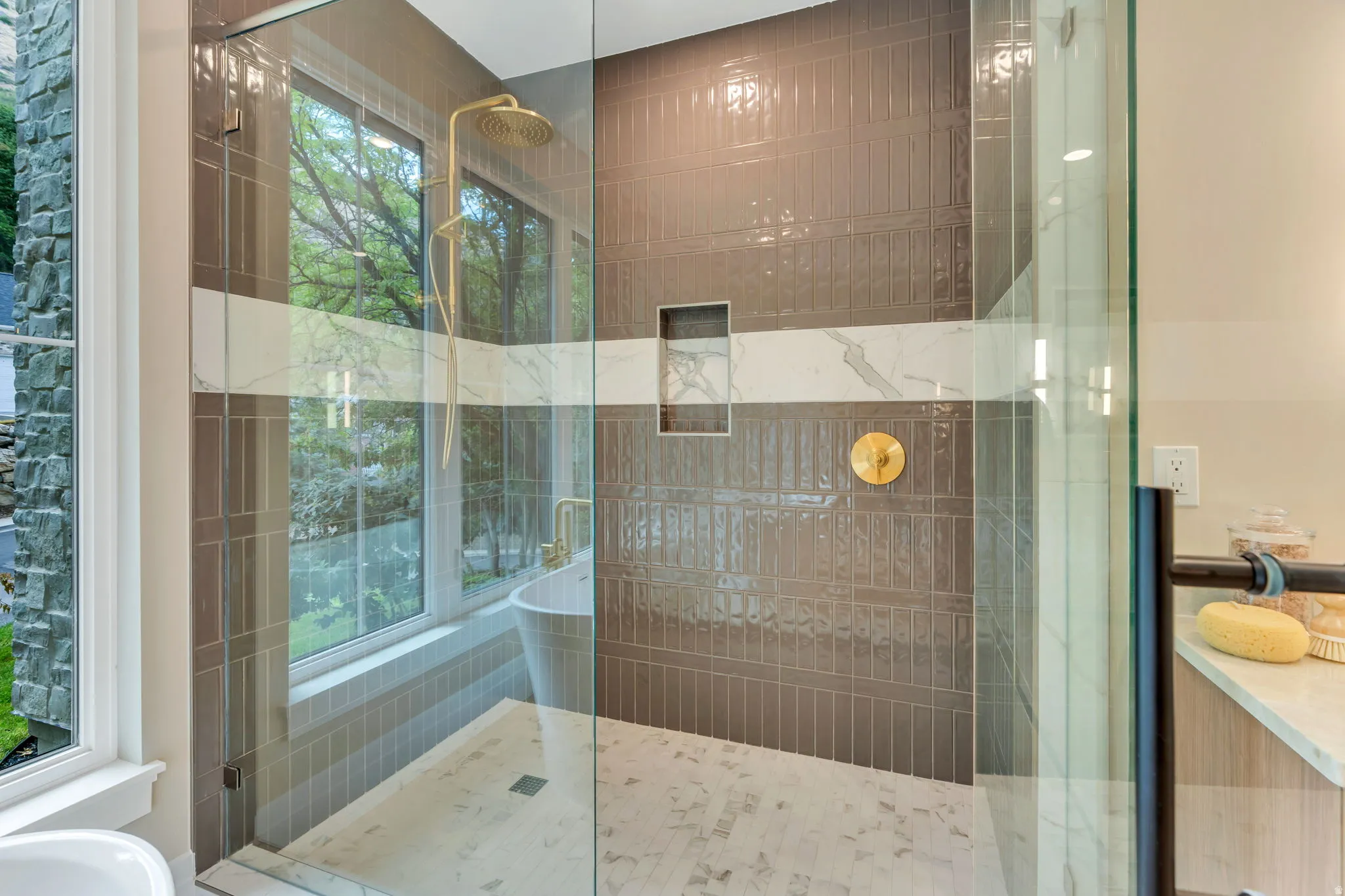 Glass-enclosed shower featuring a rain showerhead, gold-finish fixtures, and a recessed niche with a marble accent band