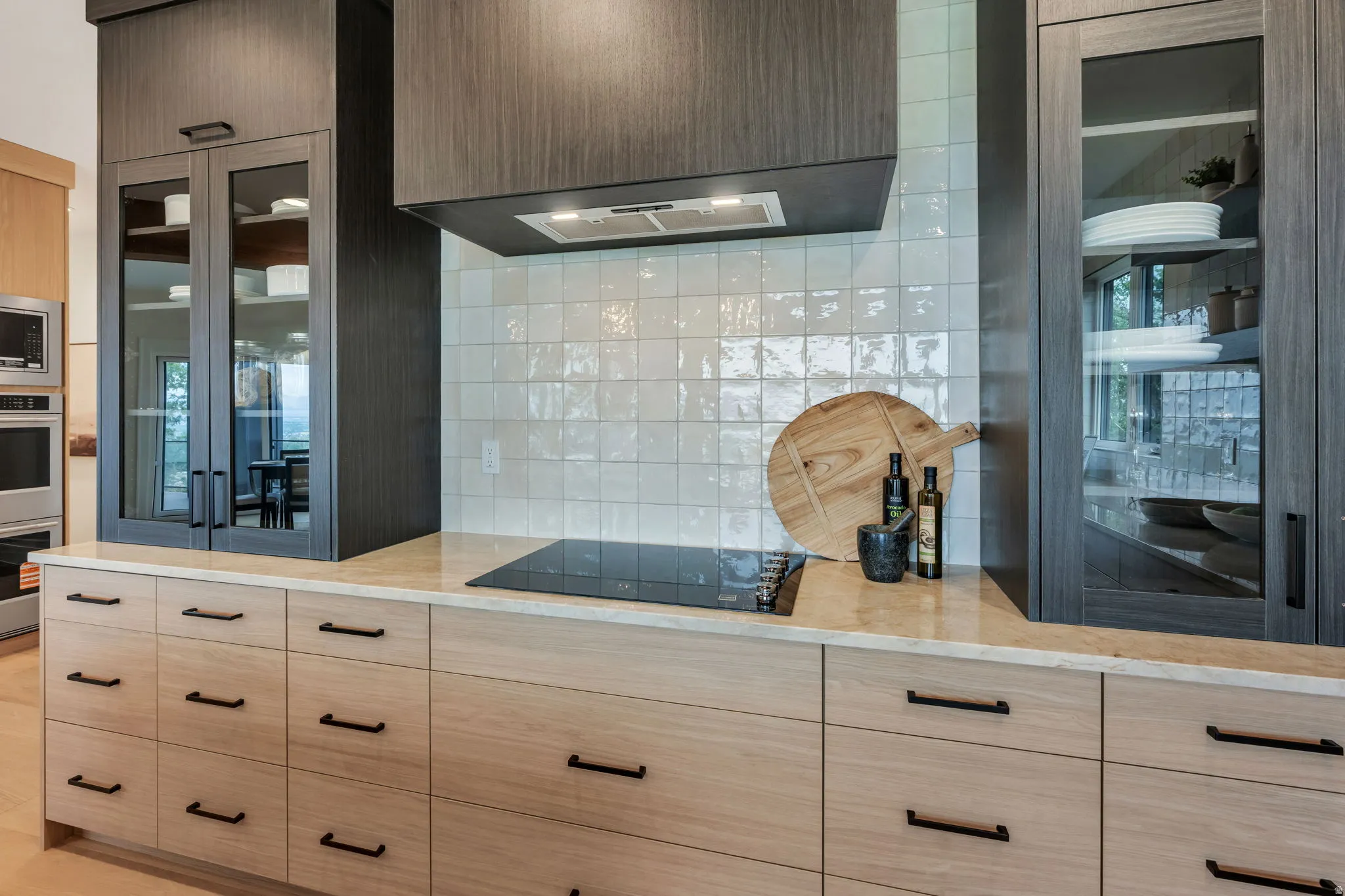 Modern kitchen featuring two-tone cabinetry, a light-toned countertop, a built-in induction cooktop, and a textured white tile backsplash