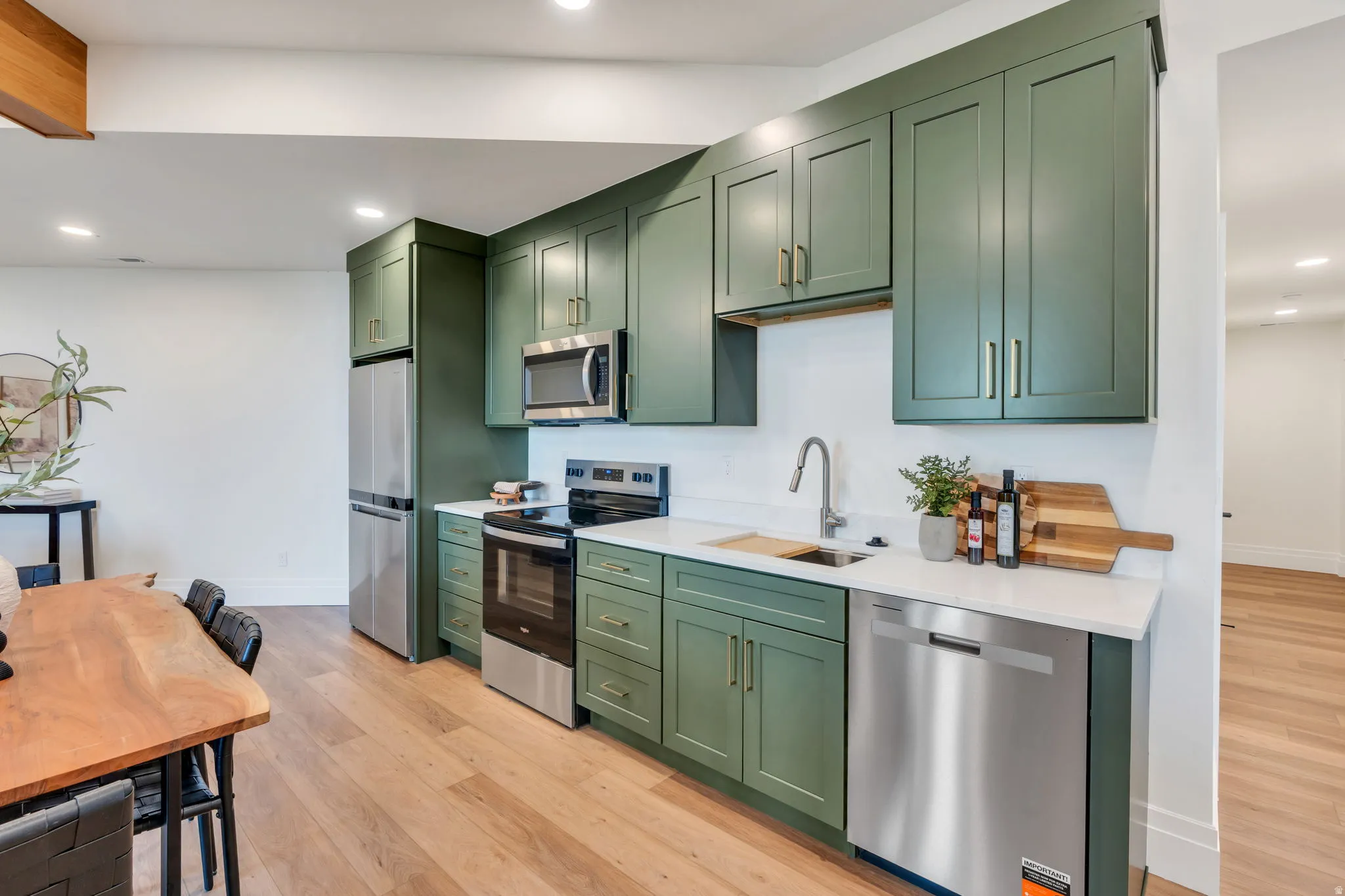 Kitchen featuring olive green cabinetry, stainless steel appliances, white countertops, and light wood-finish flooring