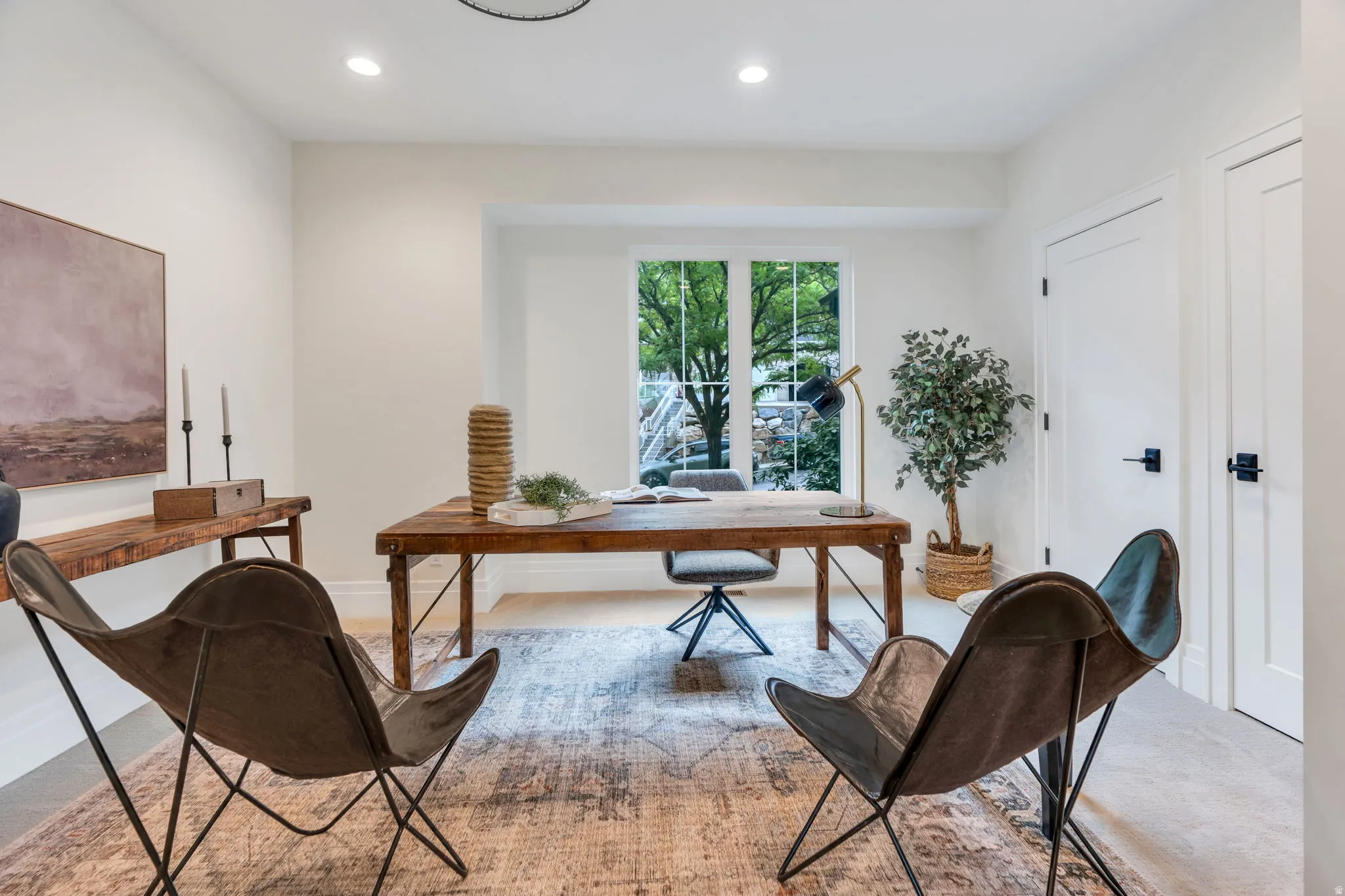 Recessed lighting illuminating a spacious room with a large window, light-toned walls, and twin paneled doors featuring black hardware