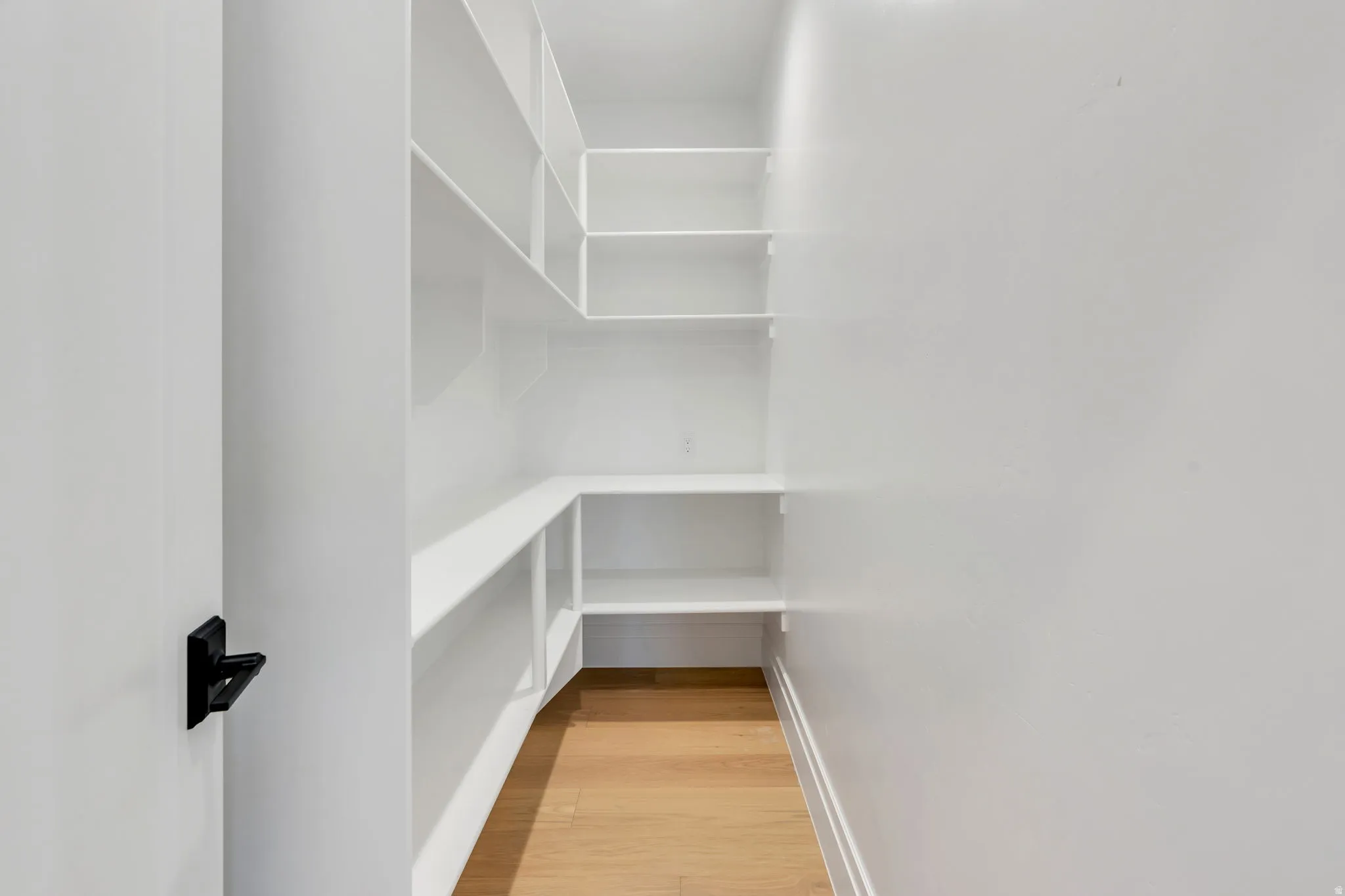 Expansive walk-in pantry featuring white built-in shelving, light wood-finish flooring, and bright overhead lighting
