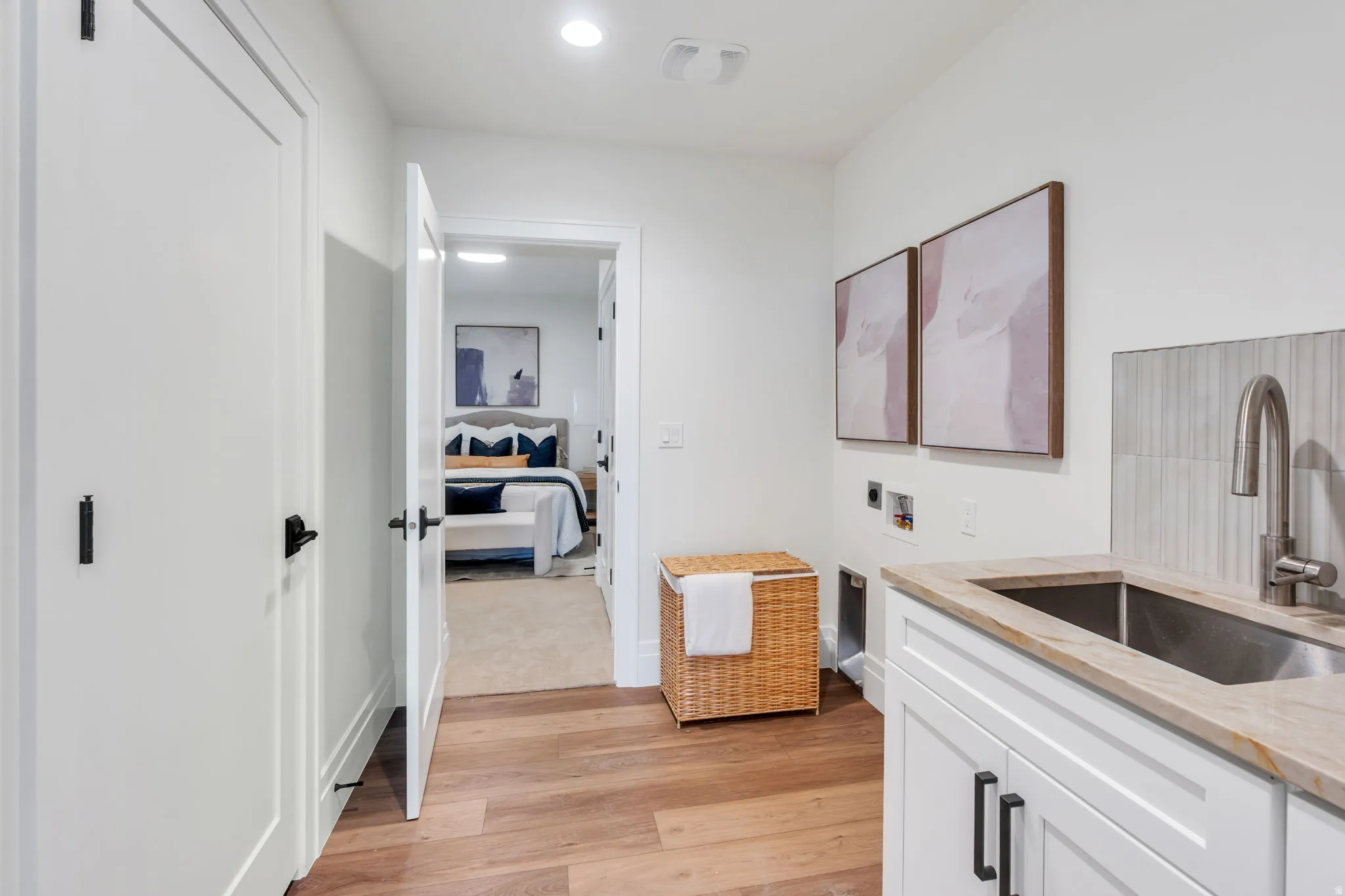 Laundry area featuring a utility sink with a stainless steel faucet, light-toned countertop, and white cabinetry with dark hardware