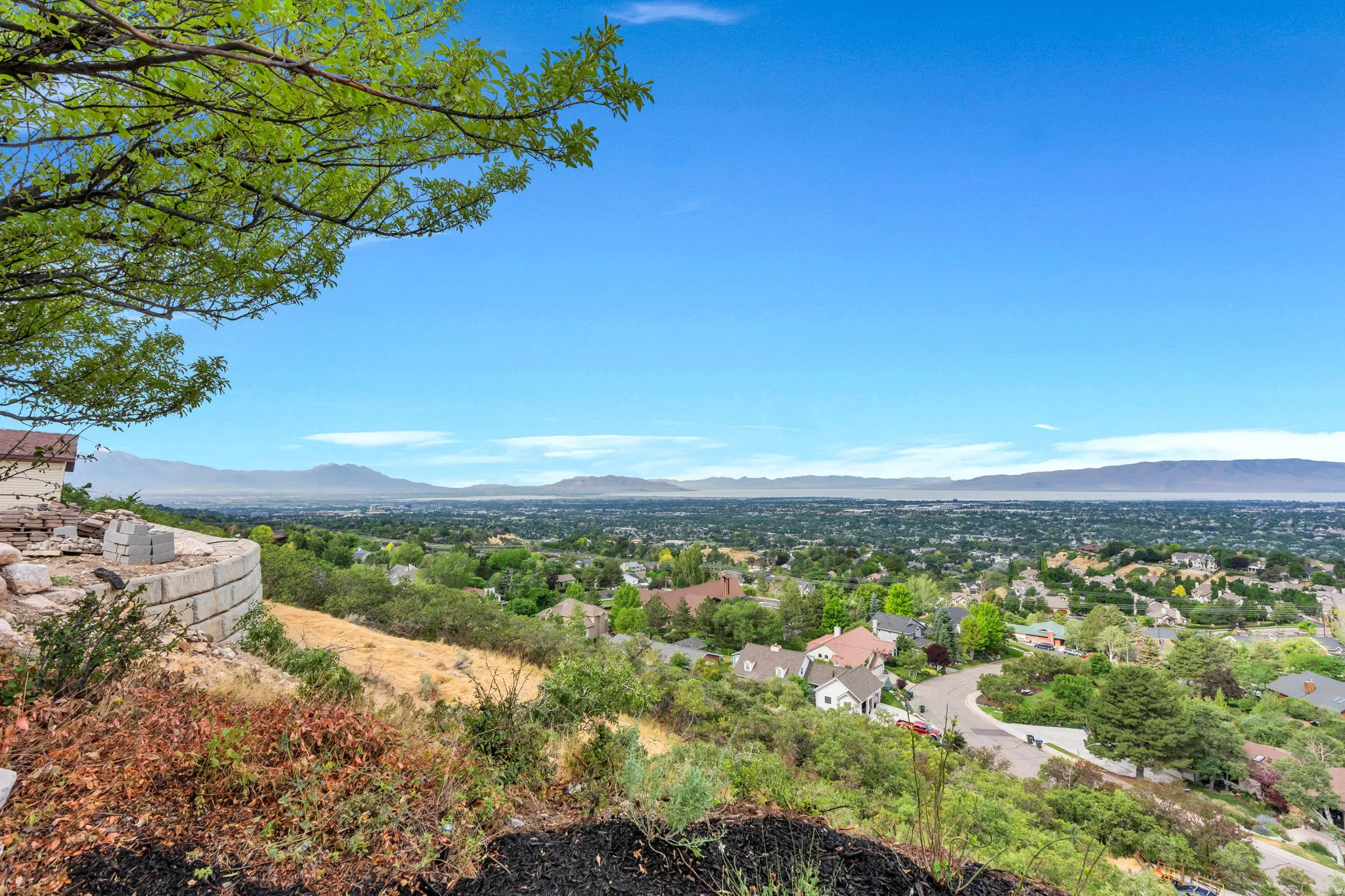 Expansive property featuring a curved retaining wall, sloped terrain, and a visible portion of a residential structure
