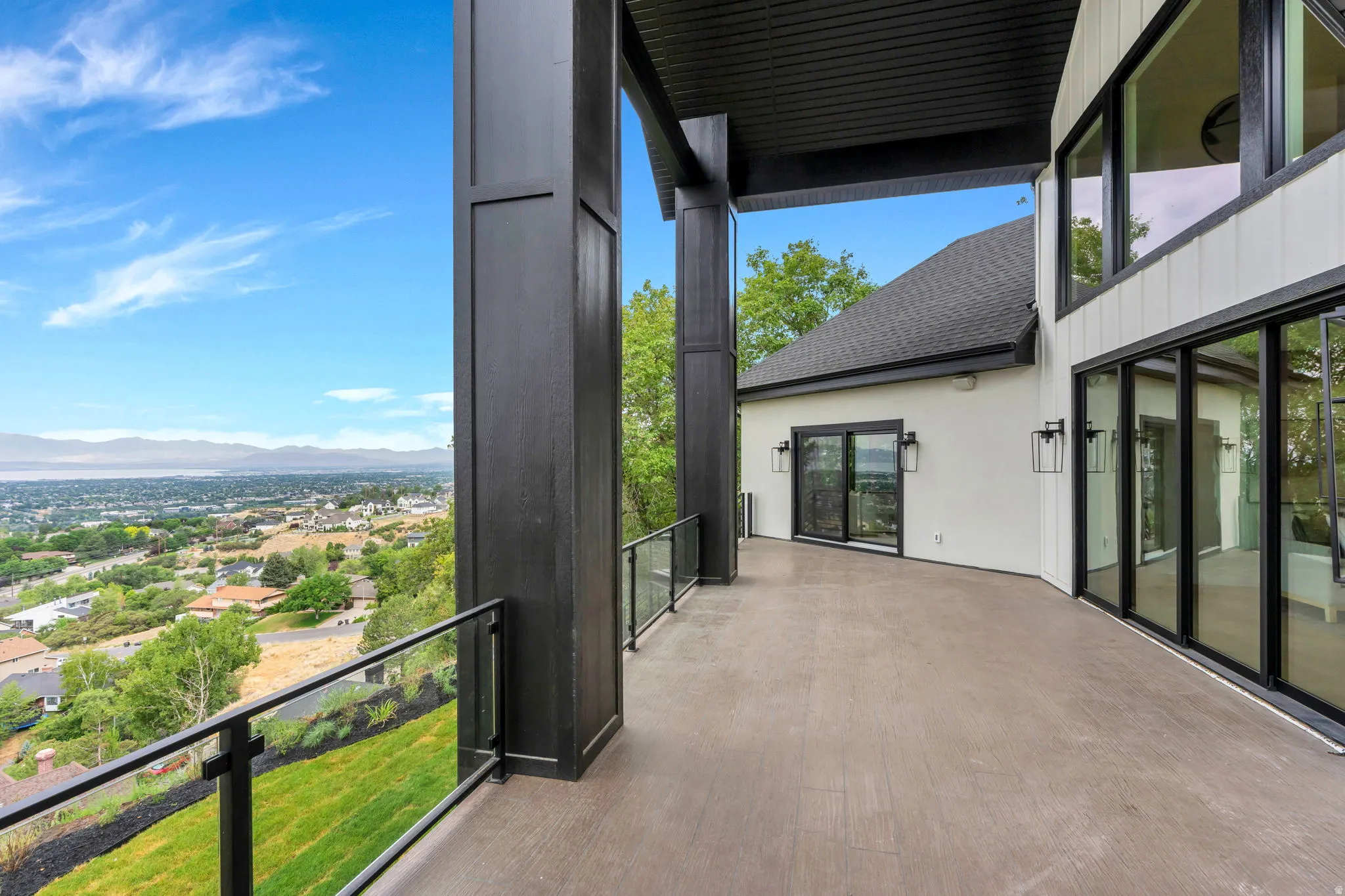 Expansive outdoor terrace featuring dark-framed glass railings, large format sliding glass doors, a smooth concrete surface, and substantial structural columns