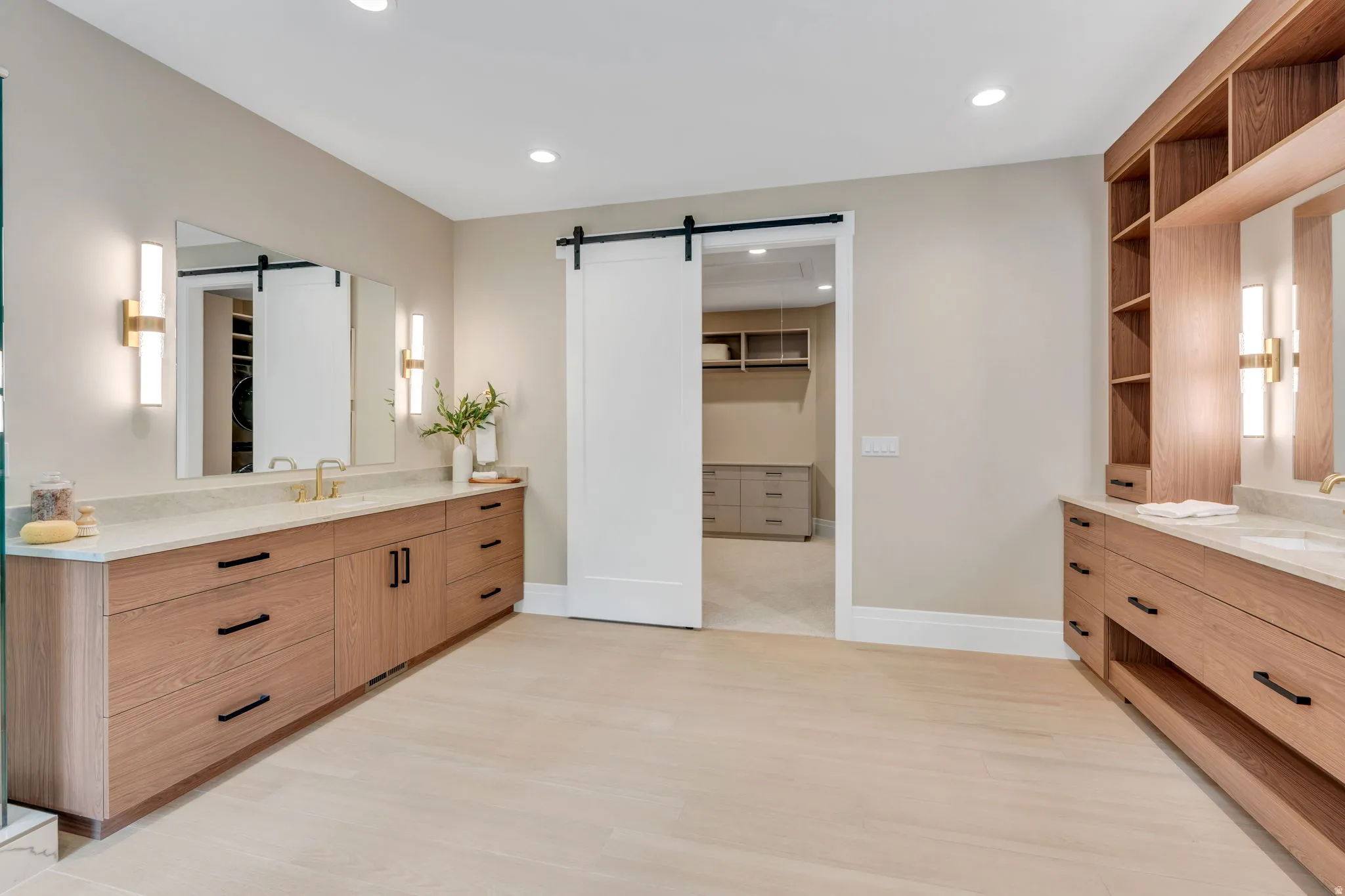 Spacious bathroom featuring twin wood-finish vanities with light-toned countertops, integrated sinks, and wall-mounted sconces