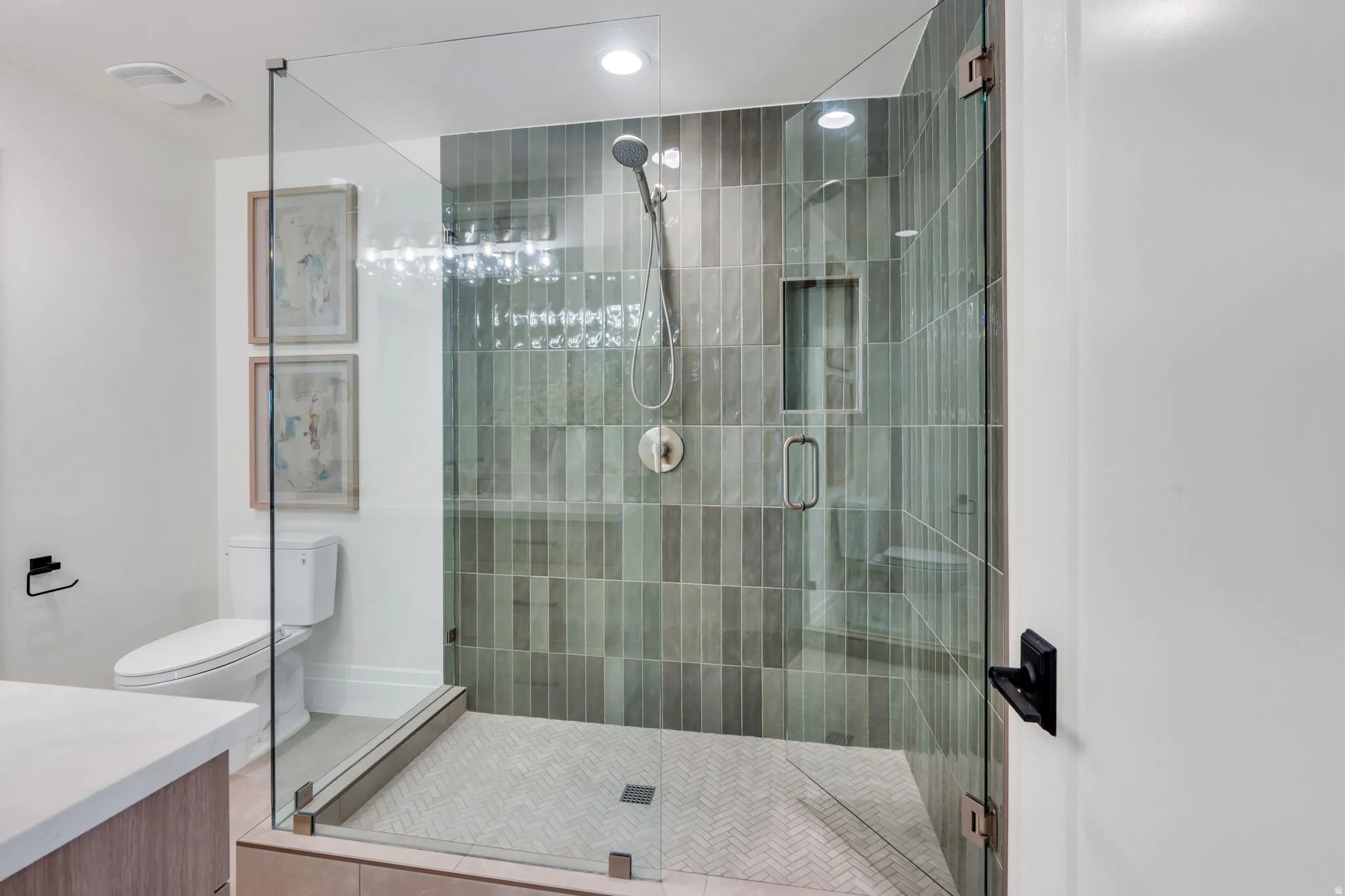 Glass-enclosed shower featuring vertical tile work in varied green tones and a built-in shower niche