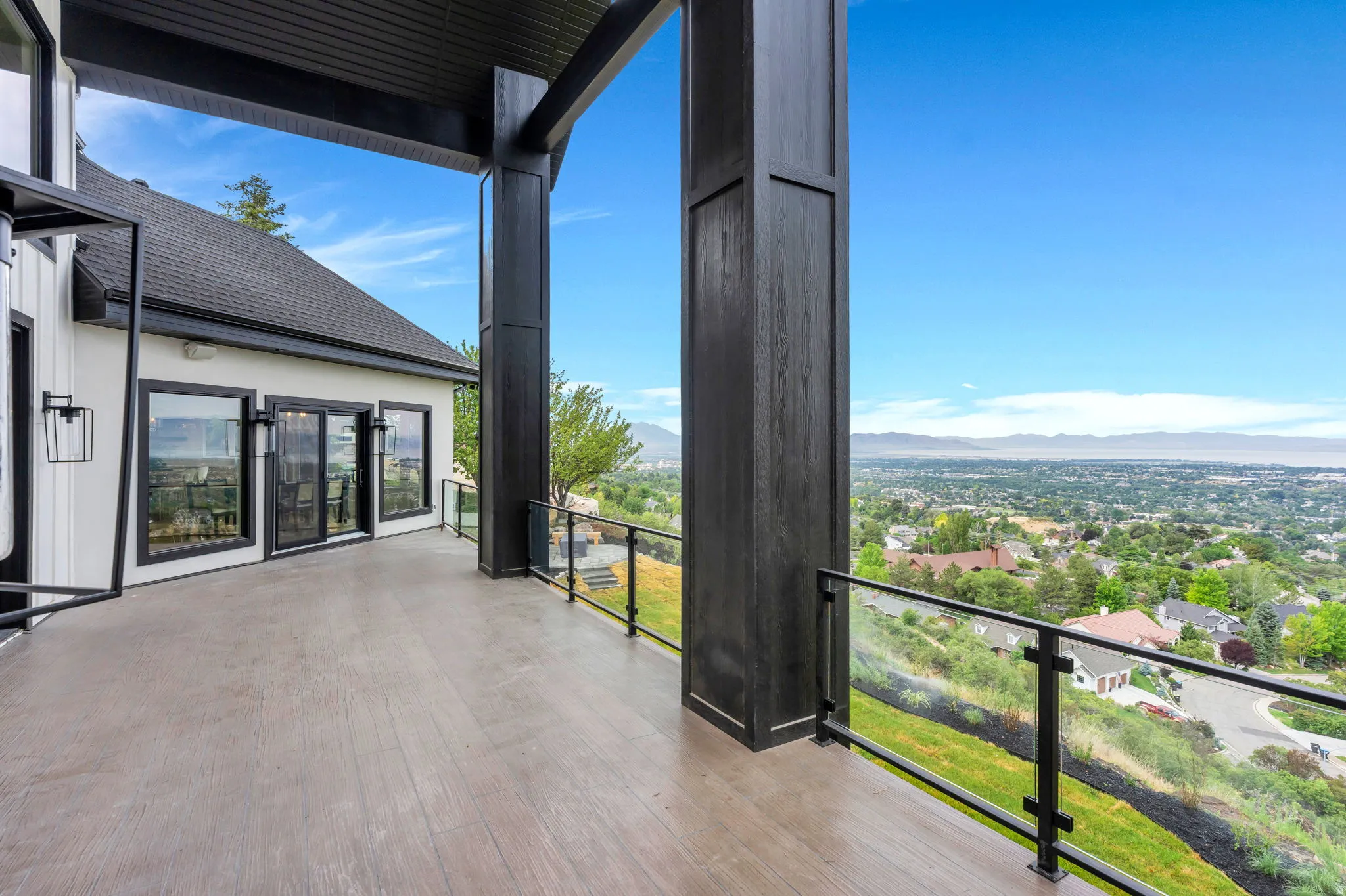 Expansive outdoor deck with wood-finish flooring, glass panel railing, and mountain-range scenery