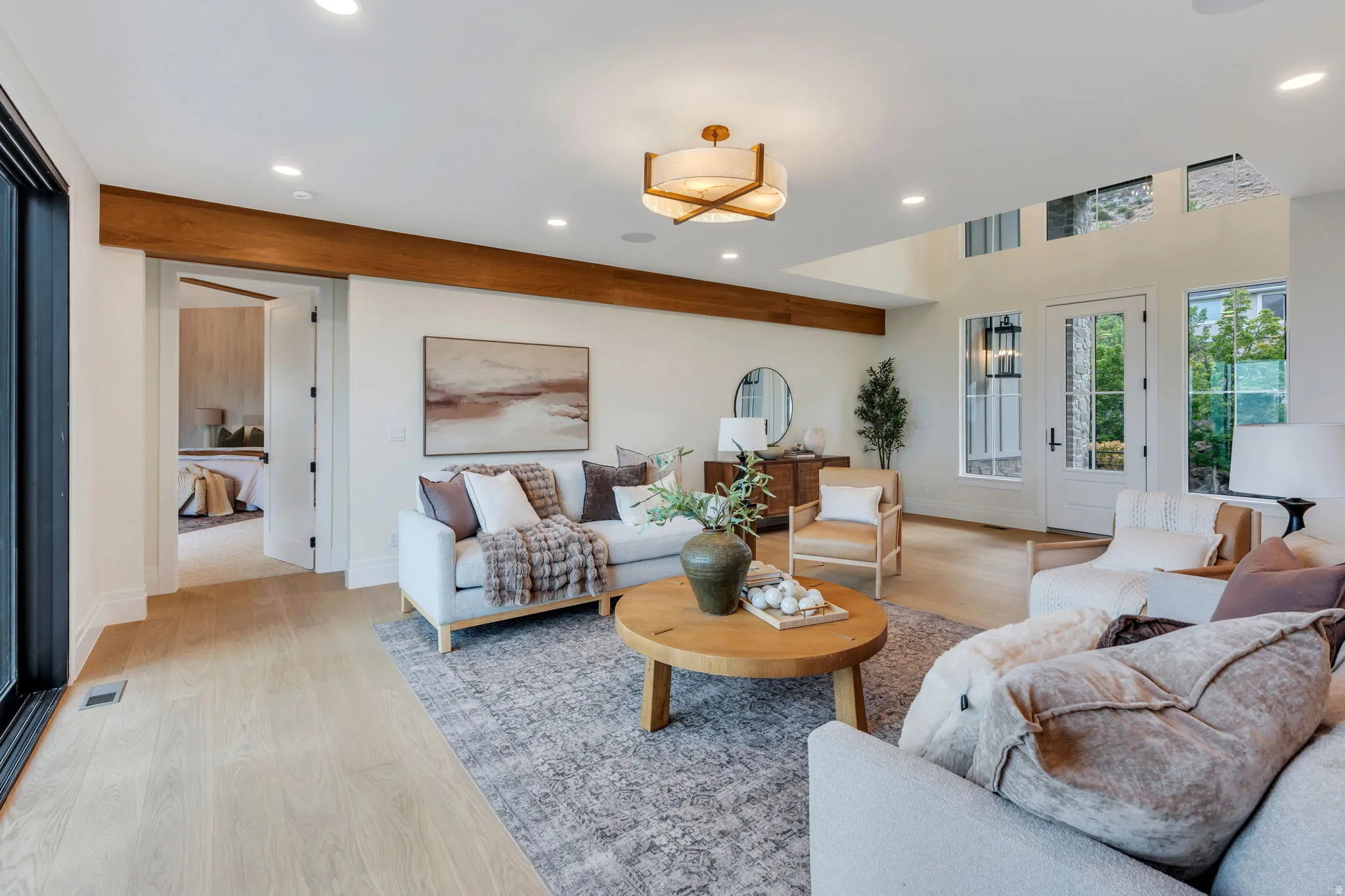 Spacious living area featuring light wood-finish flooring, a prominent exposed wood beam, recessed lighting, and a contemporary ceiling fixture