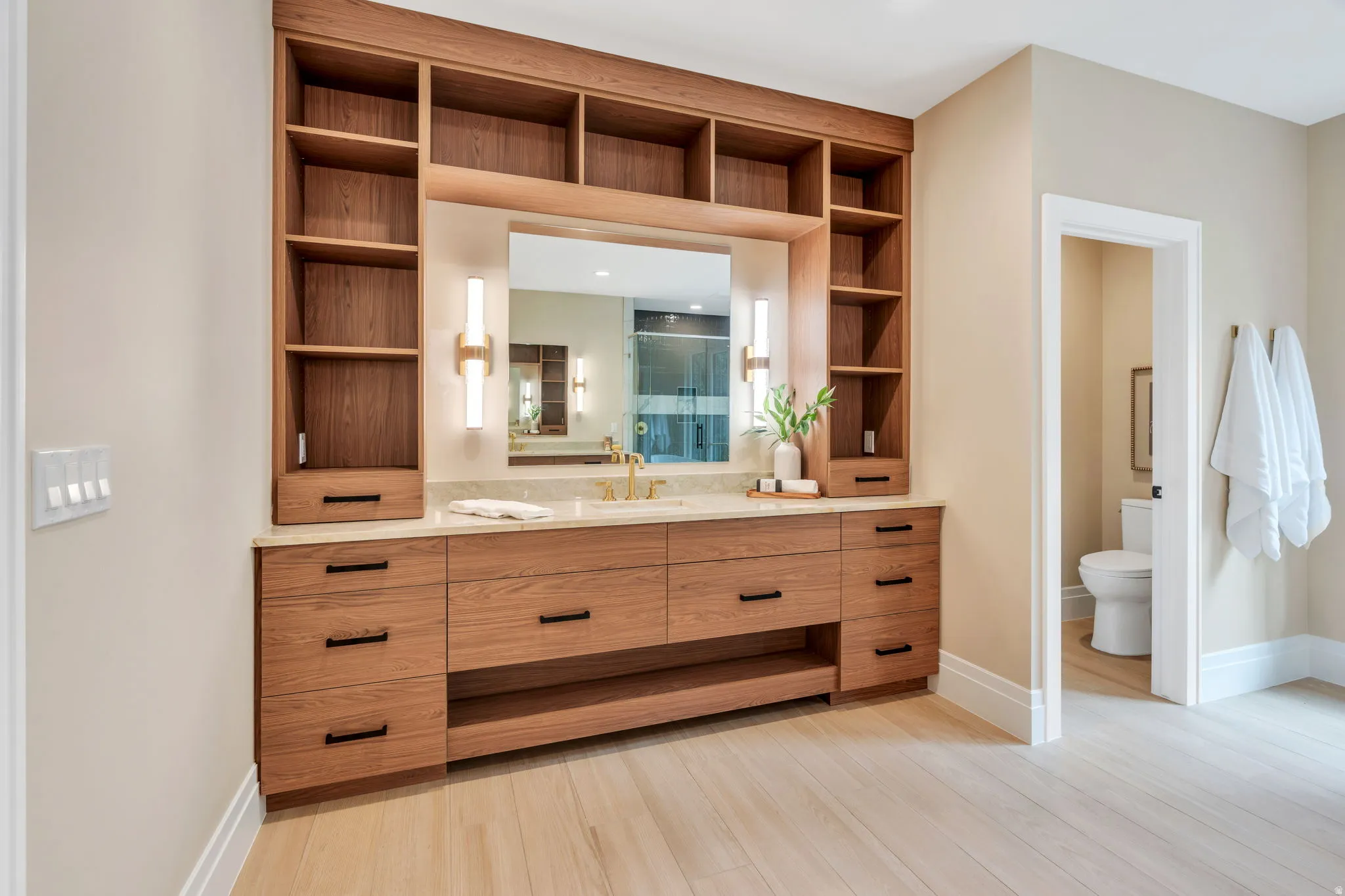 Custom wood-finish vanity with an integrated sink, stone countertop, and gold-tone fixtures