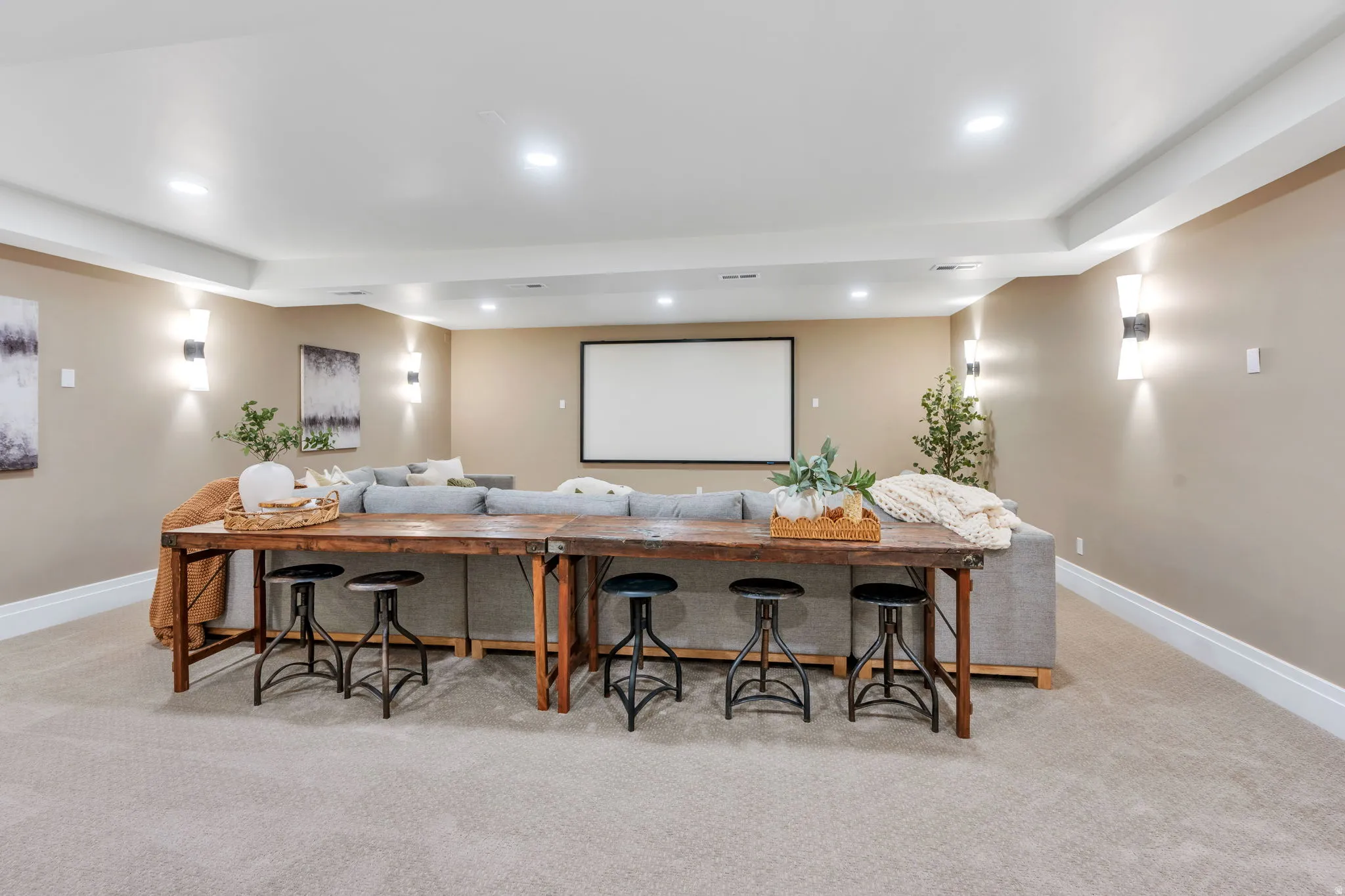 Spacious room featuring a large projection screen, recessed lighting, wall sconces, and neutral-toned carpeting